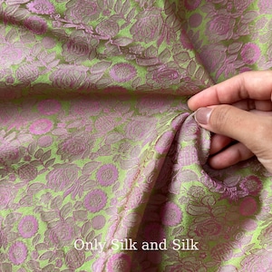 Könnte beinhalten: Nahaufnahme eines Stoffes mit floralem Muster in Grün- und Rosatönen. Das Material hat eine strukturierte Oberfläche mit einem sich wiederholenden Muster aus Blumen und Blättern. Der Text "Only Silk and Silk" ist unten im Bild zu sehen.