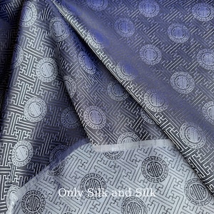 May include: Folded fabric with a repeating geometric pattern in blue and silver. The fabric has a sheen and a detailed design featuring circular motifs and linear elements. The text "Only Silk and Silk" is visible on the fabric.