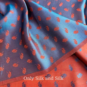 Peut inclure: Gros plan sur un tissu de soie plié avec un motif floral. Le tissu a un éclat iridescent bleu et violet avec de petits motifs orange en forme de fleurs. La couche inférieure est de couleur orange uni. Le texte "Only Silk and Silk" est visible.