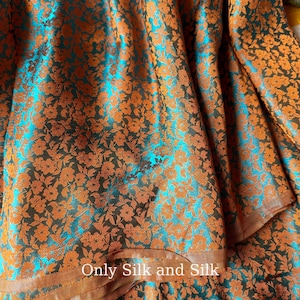 Könnte beinhalten: Nahaufnahme eines Stoffes mit floralem Muster. Der Stoff hat einen türkisfarbenen Hintergrund mit orangefarbenen Blumen. Der Text "Only Silk and Silk" ist unten im Bild zu sehen. Der Stoff scheint Seide zu sein.