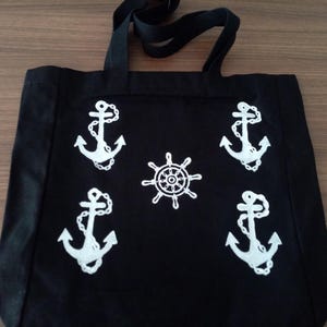 K&ouml;nnte beinhalten: Schwarze Stofftasche mit wei&szlig;en Anker- und Schiffssteuerrad-Designs.