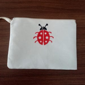 May include: A white canvas zippered pouch with a red ladybug design. The ladybug has black spots and antennae.