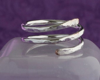 May include: A silver hammered ring with a spiral design. The ring is made of two bands of metal that are twisted together.