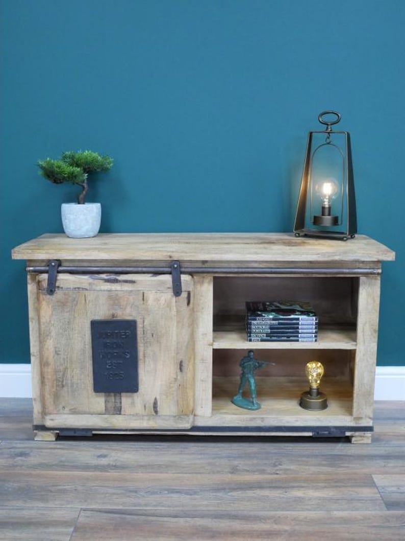May include: A light-colored wooden cabinet with a sliding door and open shelving. The cabinet has a metal plate with text and is decorated with a small bonsai tree, a lamp, and other decorative items.