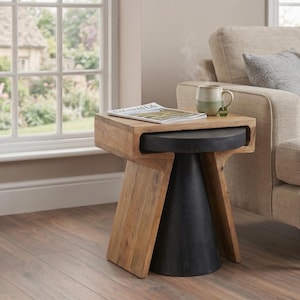 May include: A wooden side table with a natural finish and a black, cone-shaped base. A magazine and a mug with a green handle sit on top of the table. A beige sofa with pillows is in the background.