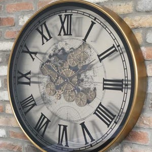 May include: A large, round, gold-framed clock with Roman numerals and a black background. The clock face features a design of gears and a world map.