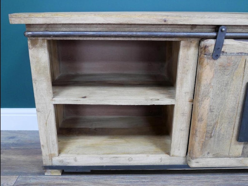 May include: A light-colored wooden cabinet with two shelves and a sliding door. The cabinet has a rustic, weathered appearance with metal hardware. The shelves are open, and the cabinet sits on a dark base.