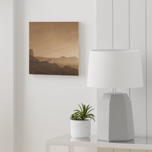 K&ouml;nnte beinhalten: Ein sepiafarbenes Foto einer Landschaft mit einem Holzrahmen. Das Foto zeigt eine felsige K&uuml;ste mit einem kleinen Boot in der Ferne. Der Himmel ist bew&ouml;lkt und die Sonne geht unter.