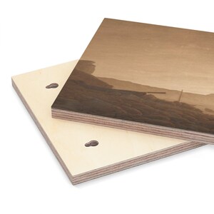 K&ouml;nnte beinhalten: Eine Nahaufnahme eines Wandbildes aus Holz mit einem sepiafarbenen Bild einer Meereslandschaft. Das Holz ist hellbraun und hat eine nat&uuml;rliche Maserung. Das Bild ist auf der Vorderseite des Holzes gedruckt und zeigt einen Strand mit Felsen und einem Boot in der Ferne.