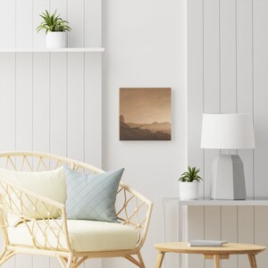 K&ouml;nnte beinhalten: Ein quadratischer Leinwanddruck mit einer Landschaftszene mit einem nebligen, goldenen Himmel und einer Silhouette einer Bergkette in der Ferne.