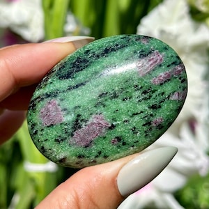 May include: A green and pink zoisite gemstone with a smooth, polished surface. The stone has a mottled pattern of green, black, and pink.