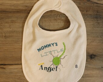 May include: A white baby bib with green, blue, and yellow embroidery. The embroidery says "Mommy's Little Angel" and has a small halo above the word "Angel". The number 8 is embroidered in the bottom right corner.