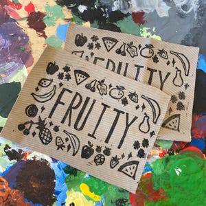 May include: Two brown fabric panels with the word "FRUITY" printed in black. The panels are decorated with black fruit and flower stamps, including apples, pears, bananas, pineapples, strawberries, and watermelon.