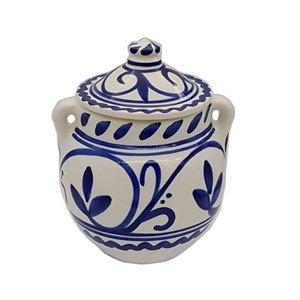 May include: A white ceramic jar with a blue and white floral design and a lid. The jar has two handles on the sides.