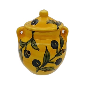 May include: Yellow ceramic jar with a lid, decorated with a hand-painted olive branch design. The jar has two handles and a small knob on the lid. The olives are black, and the leaves are green.