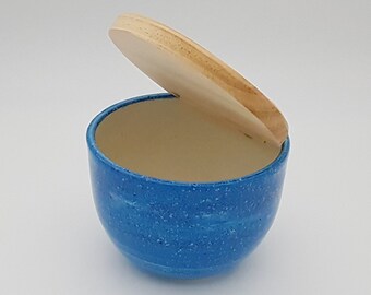 May include: A blue ceramic container with a speckled finish and a wooden lid. The lid is open and the container is empty.