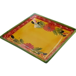 May include: A square ceramic serving platter with a yellow background and green and red floral designs. The platter has a green border with a red and white wavy line design.