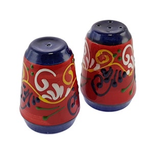 May include: A set of two red and blue ceramic salt and pepper shakers with a floral design.