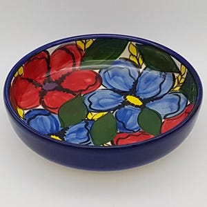 May include: A blue and white ceramic bowl with a floral design. The bowl features red, blue, green, and yellow flowers. The bowl is ideal for serving snacks or salads.