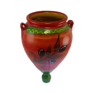 May include: Red ceramic vase with a green and yellow trim and a painted olive branch design. The vase has two handles and a rounded bottom.