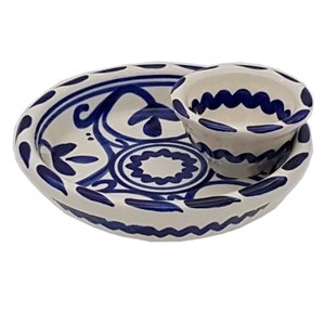 May include: A cream-coloured ceramic serving set comprising an oval platter and a small bowl, both decorated with detailed blue floral and geometric designs. The platter has a scalloped edge, and the bowl sits on top.