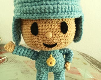 Puede incluir: Un juguete de crochet con un sombrero azul, un mono azul y un botón amarillo. El juguete tiene una cara sonriente con ojos negros y una nariz marrón.