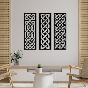 May include: Three black metal wall decor panels with a white Celtic knot design. The panels are hanging on a white wall in a living room setting.
