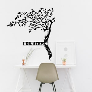 May include: Black metal wall art featuring a stylized tree with branches growing from a human spine. The tree is labeled "DR. STEVE" in a rectangular box.