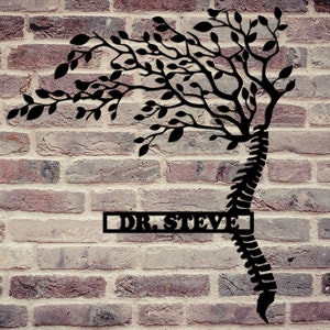 May include: Black metal wall art featuring a stylized tree with branches growing from a human spine. The art piece has a rectangular nameplate with the text "DR. STEVE" on a brick wall background.