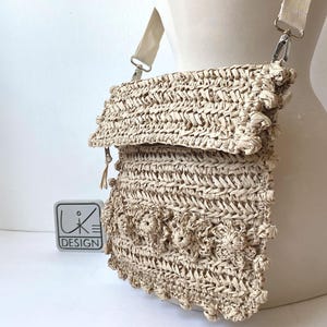 May include: A beige woven straw crossbody bag with a flap closure and a decorative flower design. The bag has a long strap and a small tassel.