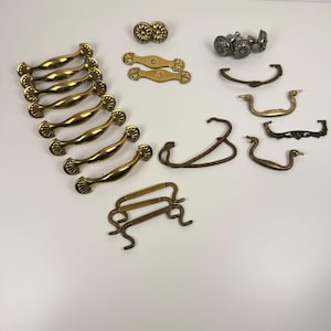 May include: A selection of antique cabinet hardware, including brass and bronze handles, knobs, and pulls. The hardware features various designs, including ornate floral and curved styles. Suitable for furniture restoration or DIY projects.