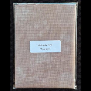 May include: Cross-stitch Aida fabric in a clear plastic sleeve. The fabric is a mottled tan colour. A white label reads "18ct Aida 19x14" and "True Grit."
