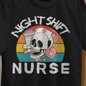 Op de afbeelding: Zwart T-shirt met een retro-grafische afbeelding van een schedel met een verpleegstersmuts en een stethoscoop. De tekst "Night Shift Nurse" is geschreven in een gotisch lettertype.