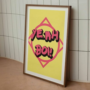 Pode incluir: Uma impressão emoldurada com fundo amarelo e uma forma de diamante rosa com o texto "YEAH BOI!" em letras pretas.