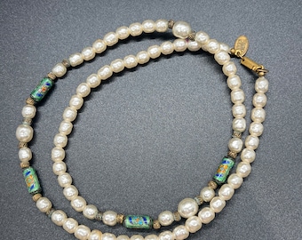 May include: A white pearl necklace with green, blue, and gold accents. The necklace has a small gold tag with the word "JADE" on it.