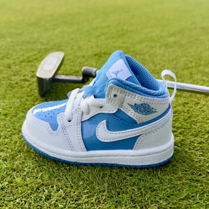 May include: A high-top sneaker in light blue and white with a patent leather finish. The shoe features a white swoosh, a white midsole, a light blue outsole, and the Air Jordan wings logo on the side. A white tongue tag displays a blue Jumpman logo.