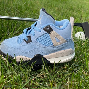 Puede incluir: Una zapatilla de bebé azul claro y gris con detalles en negro, sobre hierba verde. La zapatilla tiene una entresuela moteada, una suela negra y cordones azul claro. Un estilo popular para niños.