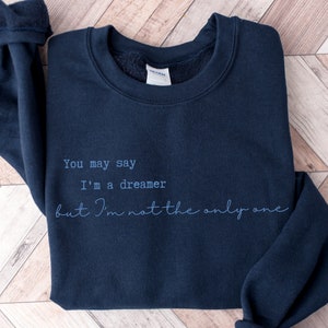 May include: A navy blue sweatshirt with the text "You may say I'm a dreamer but I'm not the only one" printed in white.