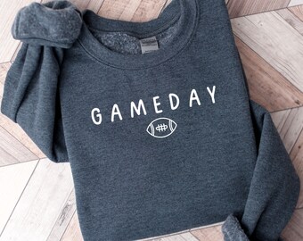 May include: A dark grey sweatshirt with the text "GAMEDAY" in white lettering and a white outline of a football below the text.