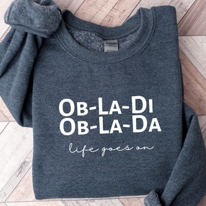 May include: A dark grey sweatshirt with the text "Ob-La-Di Ob-La-Da life goes on" printed in white.