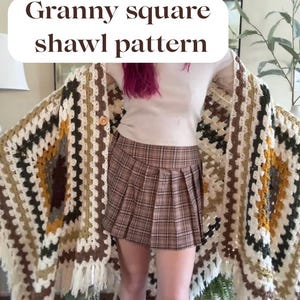 May include: A handmade granny square shawl pattern in shades of cream, brown, and gold. The shawl has a fringed edge and is draped over a person. The text "Granny square shawl pattern" is displayed on the image.