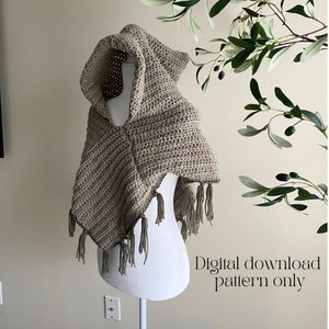Può includere: Un scialle con cappuccio lavorato a uncinetto con frange di colore marrone chiaro. Lo scialle è esposto su un manichino bianco. Il testo "Download digitale del modello solo" è visibile nell'angolo in basso a destra dell'immagine.