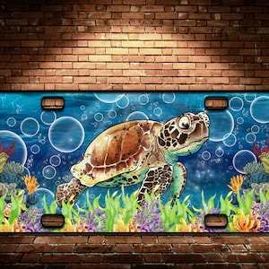 May include: License plate featuring a sea turtle swimming underwater. The design includes a brown and green turtle, bubbles, coral, and aquatic plants against a blue background. The plate has a rectangular shape with mounting holes.