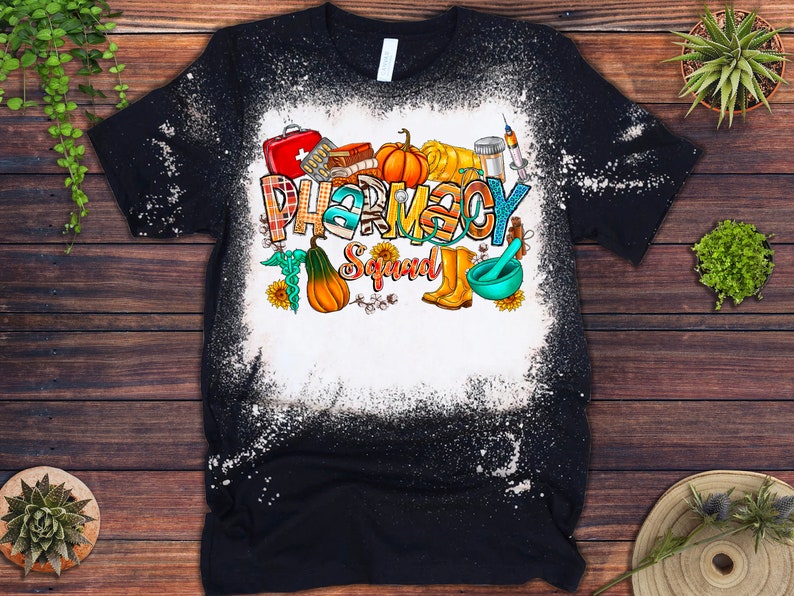 May include: Black t-shirt with a bleach-splattered design featuring a colorful graphic of the text "Pharmacy Squad" with various pharmacy-related icons and fall-themed elements like pumpkins and gourds.