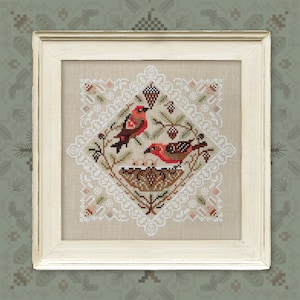 May include: A framed cross-stitch design featuring two red birds perched on a branch with a nest below. The design is surrounded by a white lace border.