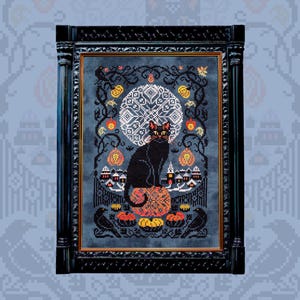 May include: A framed cross-stitch featuring a black cat with yellow eyes perched on a pumpkin. The design includes pumpkins, a full moon, and a small village, all set against a dark blue background. Two black crows are at the bottom.