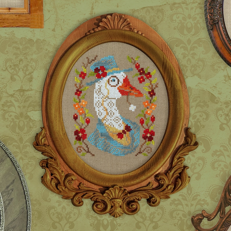 May include: A cross-stitch embroidery of a goose wearing a hat and monocle, framed in a gold oval frame with ornate details.