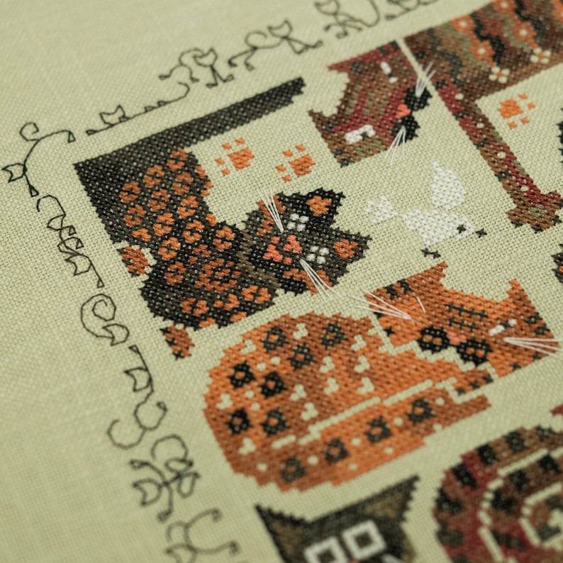 May include: A cross-stitch pattern featuring a variety of cats in different colors and patterns. The cats are arranged in a grid pattern and are surrounded by a border of small cats. The text "Our Cats" is written in a cursive font at the bottom of the pattern.