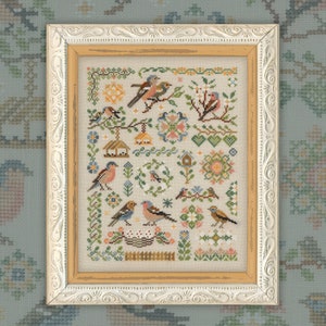 Puede incluir: Un diseño de bordado de punto de cruz con una variedad de pájaros, flores y otros motivos inspirados en la naturaleza. El diseño está enmarcado en un marco de color plateado con un passe-partout marrón claro.