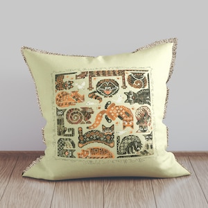 May include: A beige pillow with a brown and orange embroidered design of cats. The design features a variety of cats in different poses, including sleeping, playing, and sitting. The pillow is decorated with a brown and white trim.